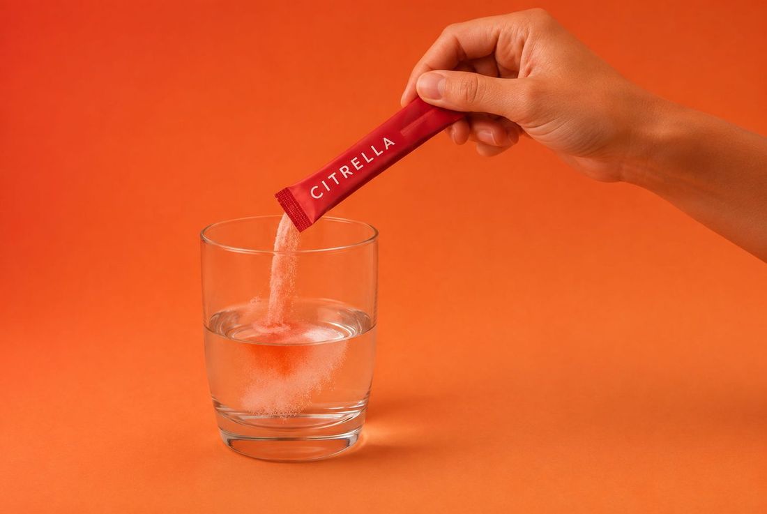 A hand emptying the powder from a Citrella sachet into a glass of water